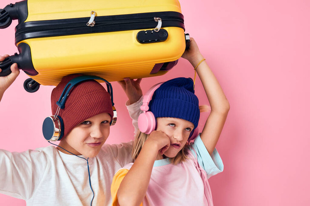 милые улыбающиеся дети с желтым чемоданом в руках розовый цвет фона - Фото, изображение