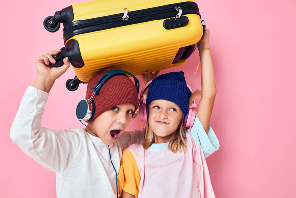 lindo sonriente niños ropa elegante maleta auriculares rosa color de fondo - Foto, Imagen