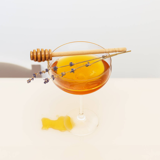 Healthcare composition with liquid honey in glass glass, lavender sprigs and honey dipper on a white table. Immune boosting food. Natural remedy for immunity and against viruses. Natural sweeteners - Fotoğraf, Görsel