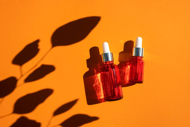 Piros üveg csepegtető ezüst fedéllel narancssárga alapon. Bőrápolási termékek gyönyörű nappali fény. - Fotó, kép