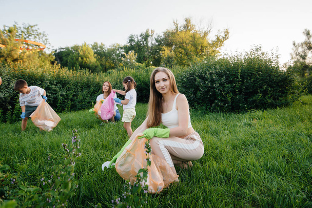 Eine Gruppe von Mädchen mit Kindern ist bei Sonnenuntergang mit der Müllabfuhr im Park beschäftigt. Umweltschutz, Recycling. - Foto, Bild