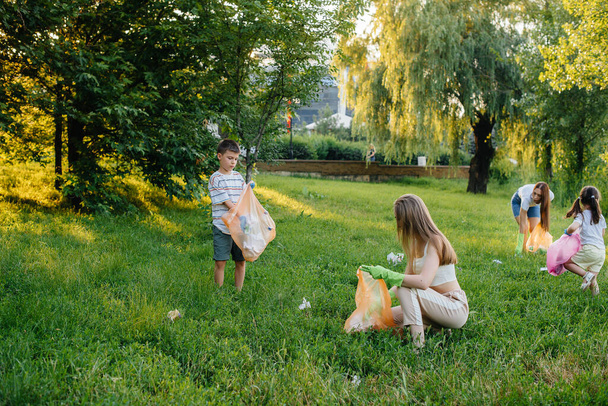 A group of girls with children at sunset are engaged in garbage collection in the park. Environmental care, recycling. - Foto, imagen