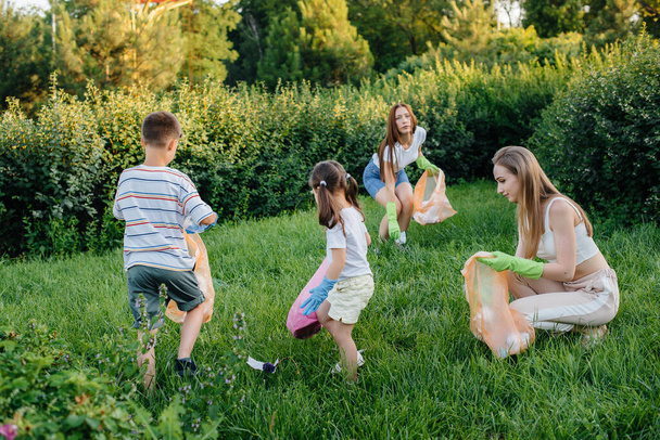 Μια ομάδα κοριτσιών με παιδιά το ηλιοβασίλεμα ασχολούνται με τη συλλογή σκουπιδιών στο πάρκο. Περιβαλλοντική φροντίδα, ανακύκλωση. - Φωτογραφία, εικόνα