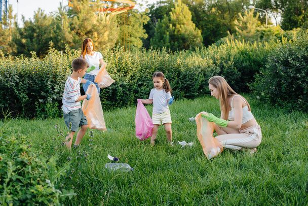 A group of girls with children at sunset are engaged in garbage collection in the park. Environmental care, recycling. - Φωτογραφία, εικόνα
