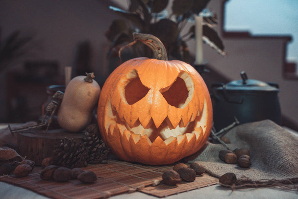 Halloween spooky pumpkin face in a table with decoration. Skeleton, candles, nuts. Teal and orange beautiful still life. - Fotó, kép