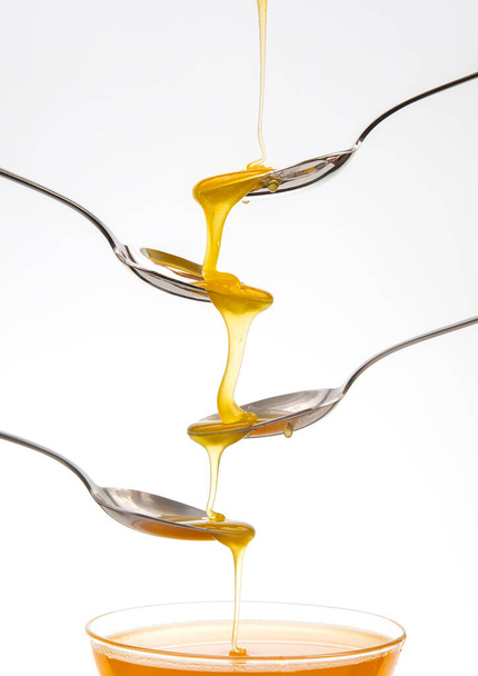 Il miele di fiore fresco gocciola da un cucchiaio in un cucchiaio su uno sfondo bianco. Alimenti vitaminici biologici. - Foto, immagini