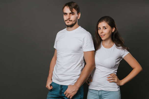 Молодая пара, женщина и мужчина в белых пустых футболках на темно-сером фоне. Мак-ап. - Фото, изображение
