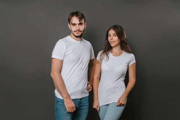 Nuori pari, nainen ja mies valkoisissa t-paidoissa tummanharmaalla pohjalla. Mallintaminen. - Valokuva, kuva