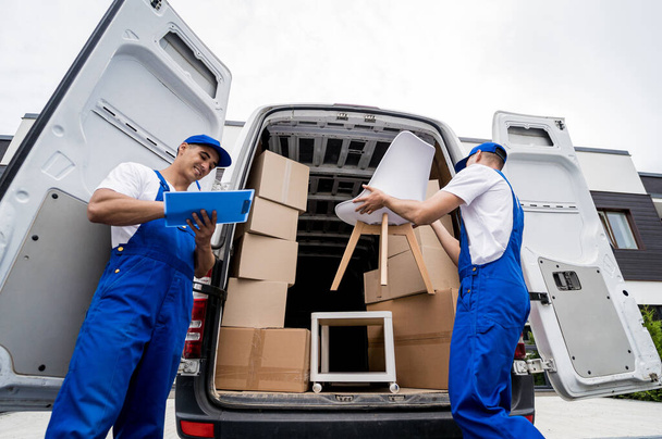 Two removal company workers unloading boxes and furniture from minibus - Photo, image