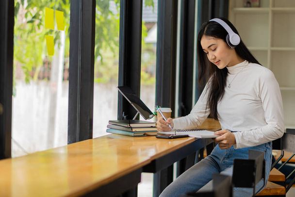 Asian teenage girl wearing headphones studying online with internet chatting teacher exam preparation white girl student learning online watching the web with laptop distance education concept - Photo, Image