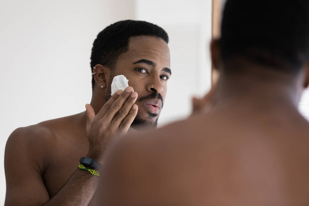 African man looking in mirror applying shaving foam on face - Foto, Bild