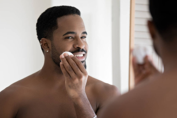 African shirtless man cleaning facial skin with cleanser lotion - Fotografie, Obrázek