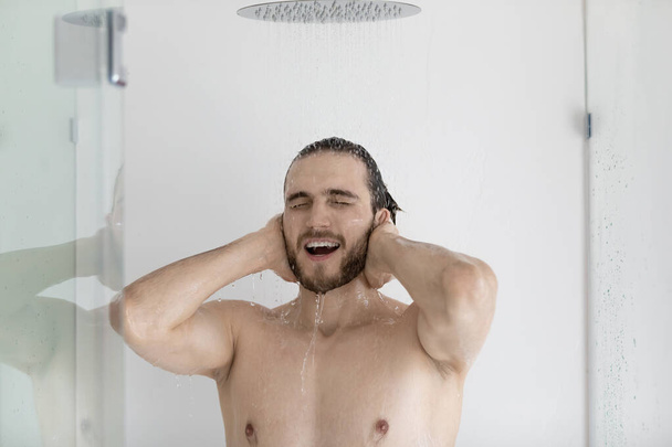 Man standing under falling water taking shower - Фото, изображение