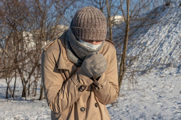 un hombre sintió frío. se vistió con un abrigo de moda, sombrero y guantes congelados. calienta sus manos con su aliento - Foto, imagen