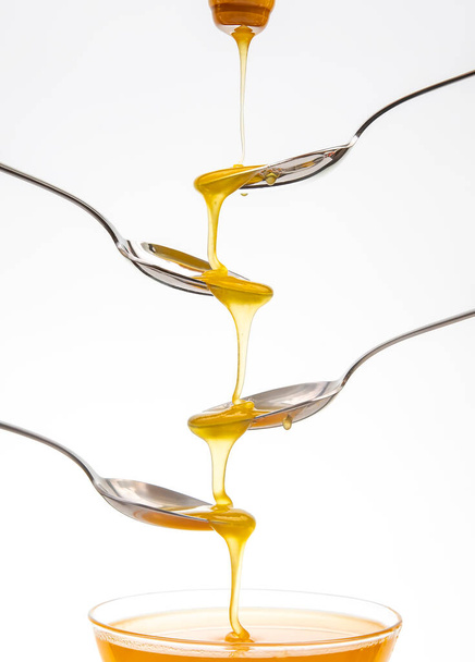 Fresh flower honey drips from a spoon into a spoon on a white background. Organic vitamin food. - Photo, image