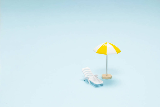 Reisconcept. Ligstoel, gele paraplu op een blauwe achtergrond. Kopieerruimte.  - Foto, afbeelding