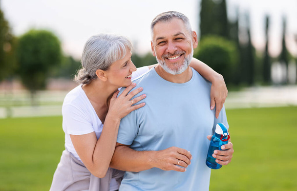 Portrait of lovely happy elderly couple on morning run outside in city park, retirees wife and husband rejoice in active lifestyle, smiling woman tenderly embracing her spouse after routine jogging - Foto, immagini