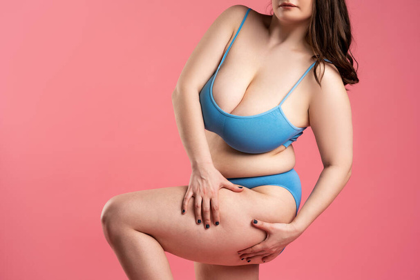 Fat woman with cellulite on thighs in blue underwear on pink background, body care concept, studio shot - Foto, afbeelding