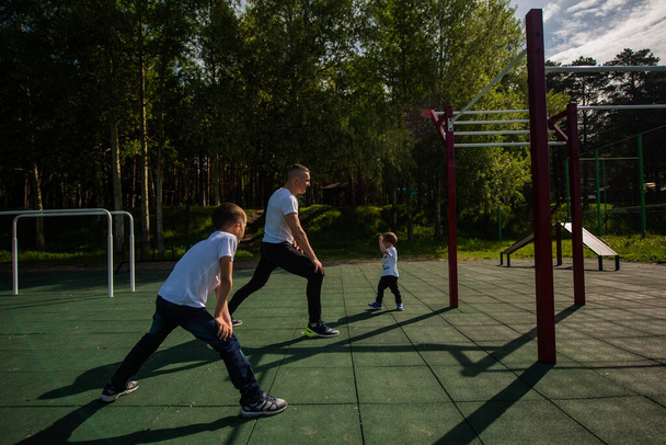 Caucasian man and two boys doing exercises outdoors. Father and sons train on the sports ground - Φωτογραφία, εικόνα