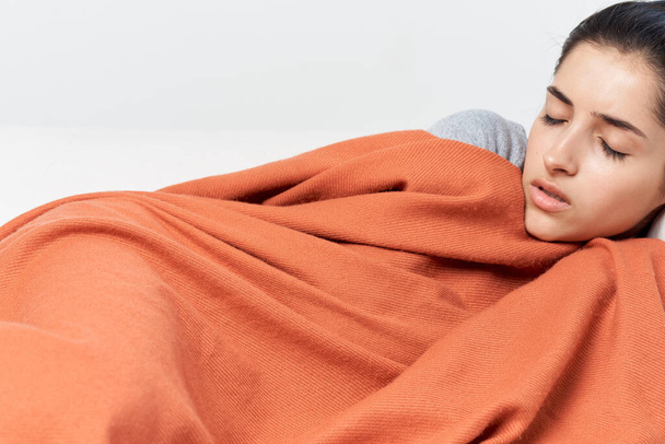 γυναίκα ξαπλώνει στο σπίτι στον καναπέ σκεπασμένη με μια κουβέρτα με κλειστά μάτια κρύα - Φωτογραφία, εικόνα