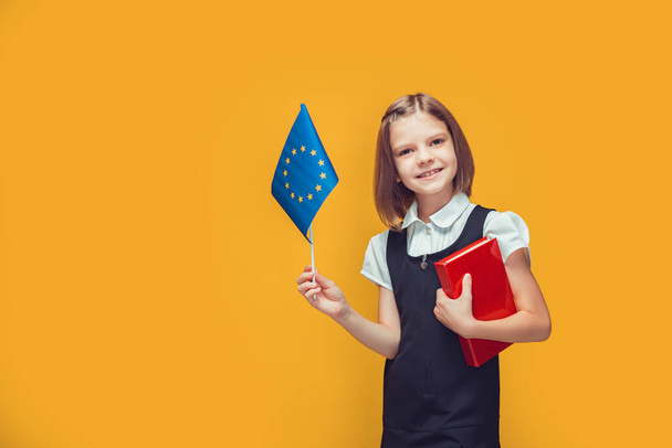 Schoolgirl holding European Union flag and book in her hands. Education in Europe concept  - Φωτογραφία, εικόνα