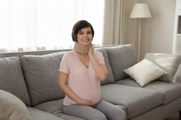 Woman having advanced pregnancy sit on sofa in medical collar - Fotoğraf, Görsel