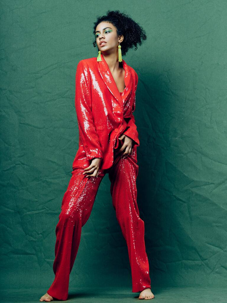 woman in a red suit on a green background in full growth looks to the side hairstyle model - Fotó, kép