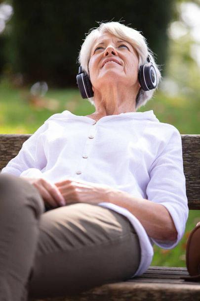 senior woman listening to music while relaxing in park - Foto, imagen