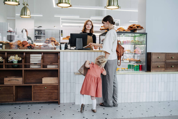 Mother with her daughter paying for pastry in a bakery shop. Girl is very restless and impatient. - Foto, Bild