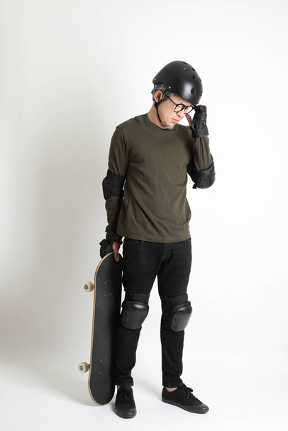 L'uomo asiatico con attrezzatura protettiva e skateboard in piedi sullo sfondo bianco. - Foto, immagini