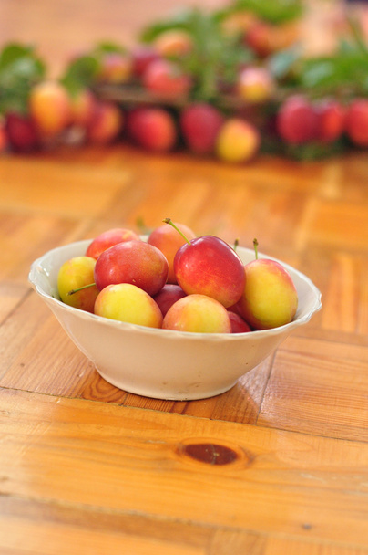 Plate of plums stands on wooden floor on blurred background - Photo, Image