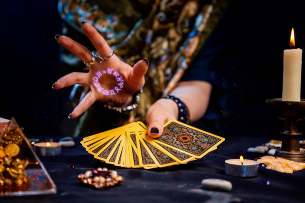 A cartomante segura um fã de cartas em suas mãos e lança um feitiço com a mão com a imagem do círculo do zodíaco. Close-up. O conceito de adivinhação, magia e esoterismo. - Foto, Imagem