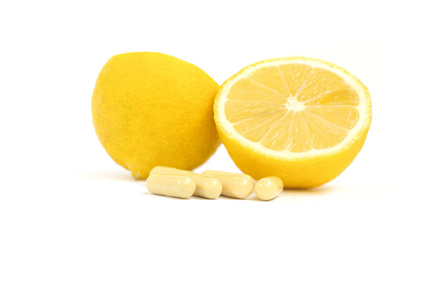 Vitamine capsules. Vitamine C pillen en gele citroen op witte achtergrond. - Foto, afbeelding