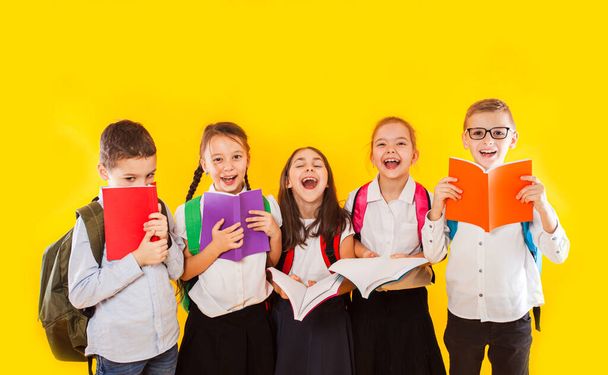 Happy schoolkids standing with colorful books isolated on yellow background. Kids hiding face behind books - Foto, afbeelding