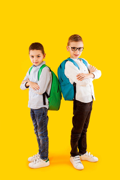 Cute schoolboys in uniform with backpacks on yellow background - Фото, зображення