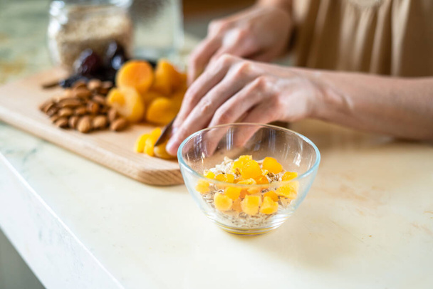female hands cut dried fruits, nuts with knife on wooden cutting board into bowl - Foto, Imagen