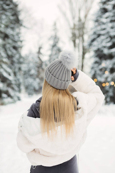 Belle femme blonde en manteau blanc regardant vers la forêt d'hiver - Photo, image