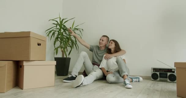 Jong stel op de vloer in een nieuwe flat. Man en vrouw in de twintig zitten op de vloer van een nieuw appartement te praten en te plannen. Real-time, hand-held schot, medium schot, 4K. - Video