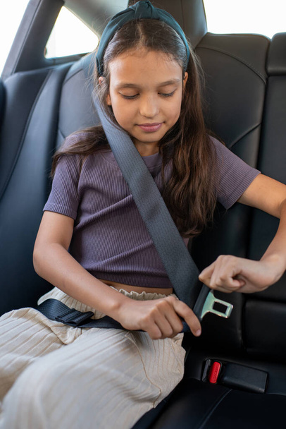 Gelukkig schoolmeisje bevestiging gordel in auto - Foto, afbeelding