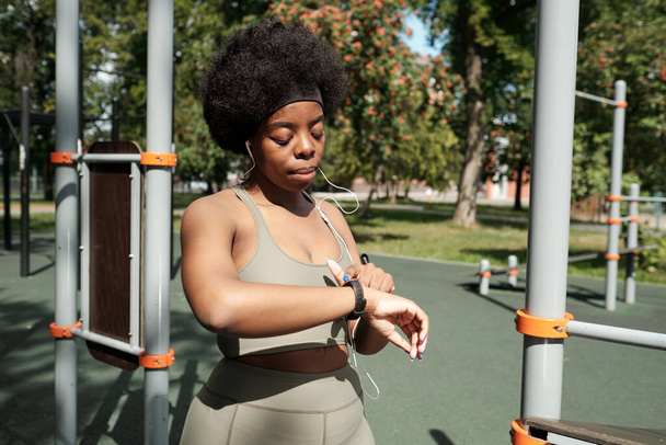 Молодая спортсменка указывает на умные часы во время тренировки - Фото, изображение