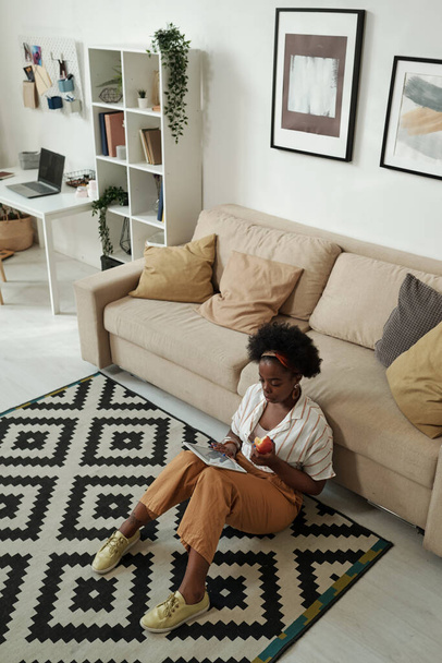Contemporary young woman using tablet while sitting on the floor by couch - Foto, Imagem