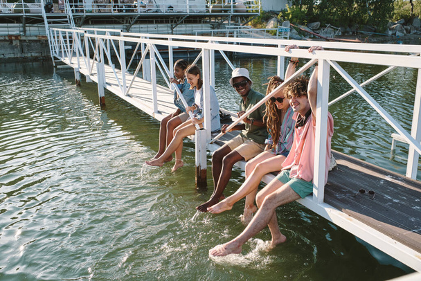 Skupina mladých bezstarostných přátel relaxovat na mostě a stříkající vody - Fotografie, Obrázek