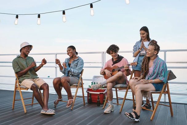 Group of young cheerful friends relaxing on pier - 写真・画像