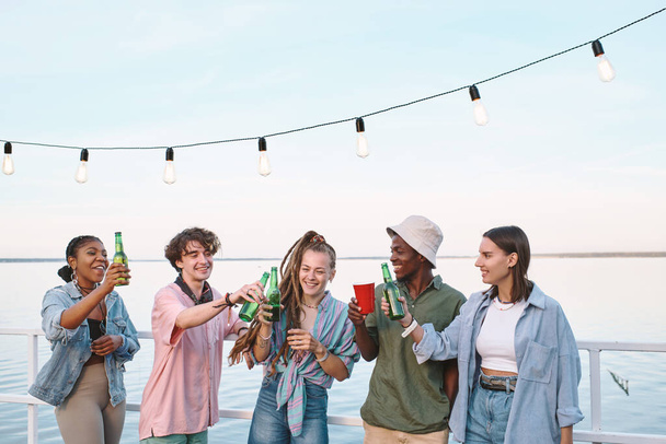 Genç neşeli arkadaşlar açık hava partisinde içkiyle kadeh kaldırıyorlar. - Fotoğraf, Görsel