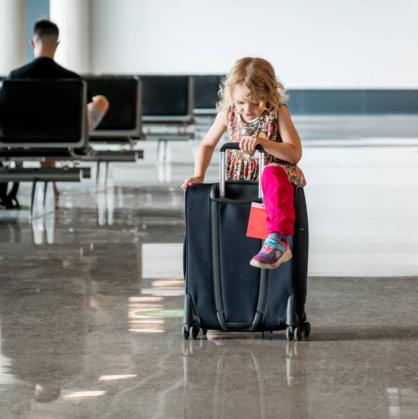 Χαριτωμένο ξανθό κορίτσι με ταξιδιωτικές αποσκευές στο αεροδρόμιο. - Φωτογραφία, εικόνα