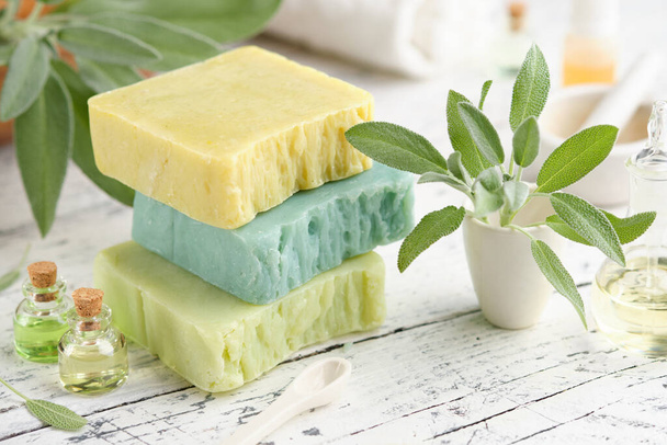 Homemade natural organic soap bars, bottles of essential oil and fresh green sage leaves on white table.  - Photo, image