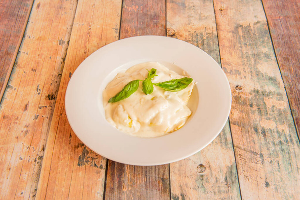 Ravioli stuffed with cheese covered with  sauce and basil leaves on wooden table - Photo, Image