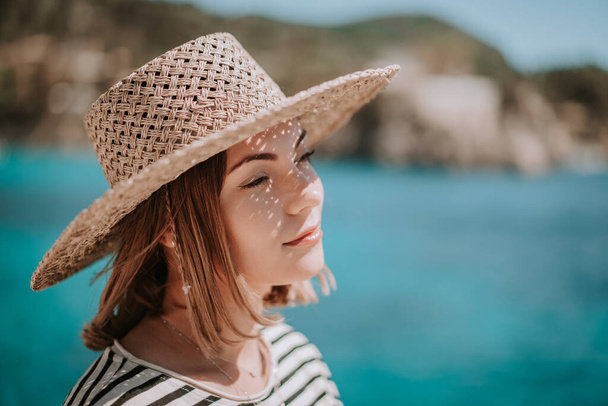 Pretty woman in straw hat smiling sincerely on blue sea background. Girl enjoying fresh air, breeze. Lady on luxury travel destination, vacation lifestyle concept. - Photo, image