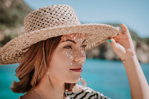 Όμορφη γυναίκα με ψάθινο καπέλο χαμογελώντας ειλικρινά στο φόντο της γαλάζιας θάλασσας. Το κορίτσι απολαμβάνει καθαρό αέρα, αεράκι. Lady on luxury travel destination, διακοπές. - Φωτογραφία, εικόνα