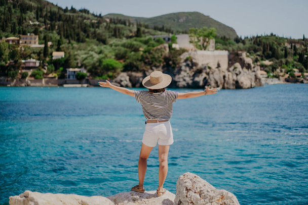 Happy carefree woman in straw hat standing on turquoise sea bay background and enjoying vacation. Girl with open arms. Travel destination, amazing nature, south Europe. - Fotoğraf, Görsel